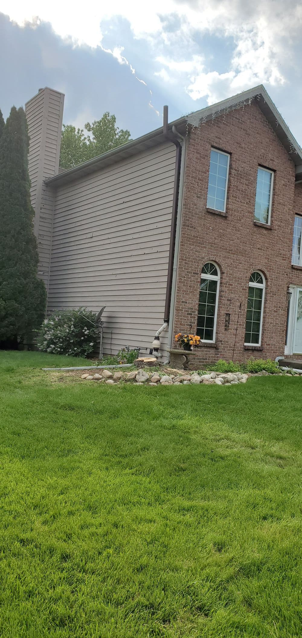 Brick house exterior with large windows, landscaped garden, and green lawn.