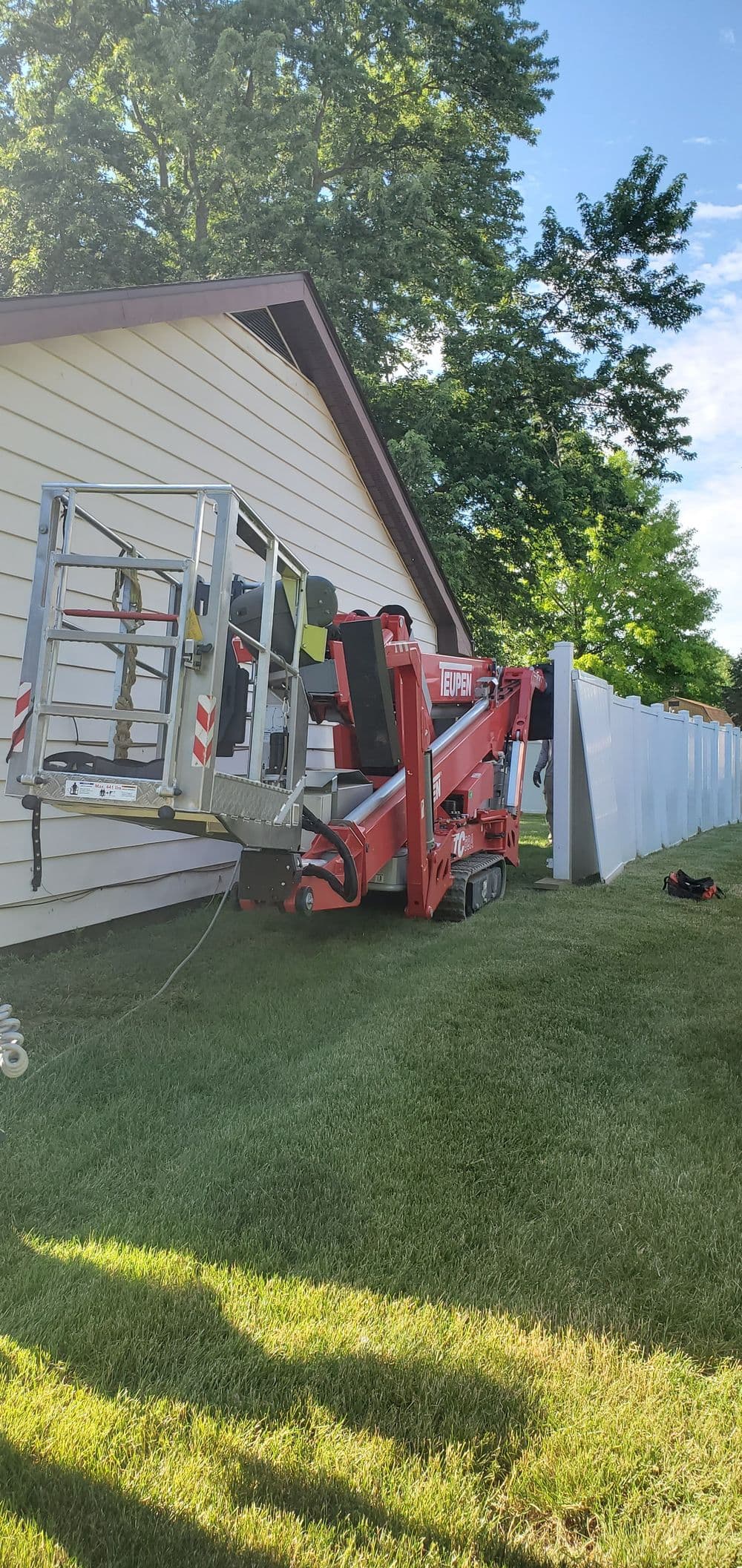 Red telescopic boom lift positioned against a house for exterior maintenance work.